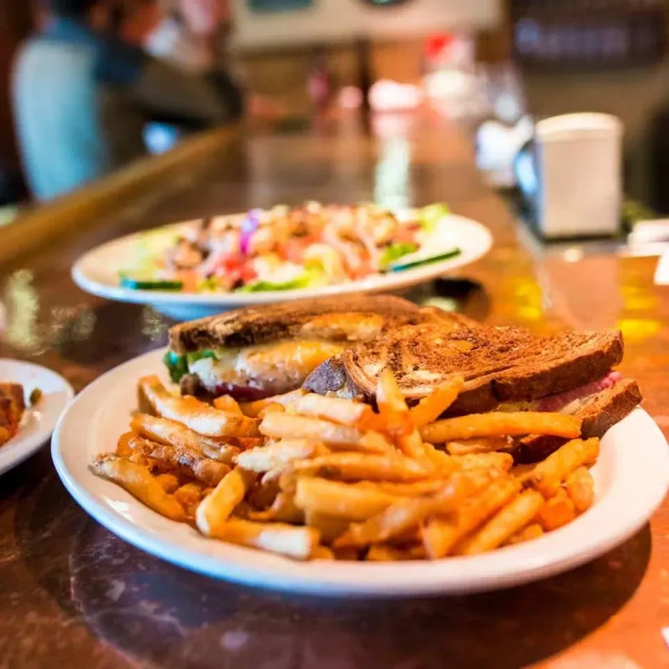 Plate with French fries, grilled cheese sandwich, and meatloaf with gravy; in the background, a salad on a plate, and a bar setting.