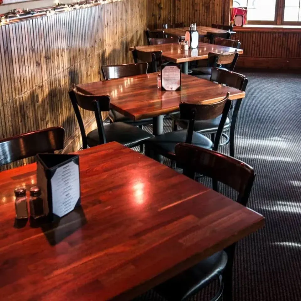 Empty dining area in a restaurant with wooden tables and chairs, menu cards, salt and pepper shakers on the tables, and a window with sunlight.